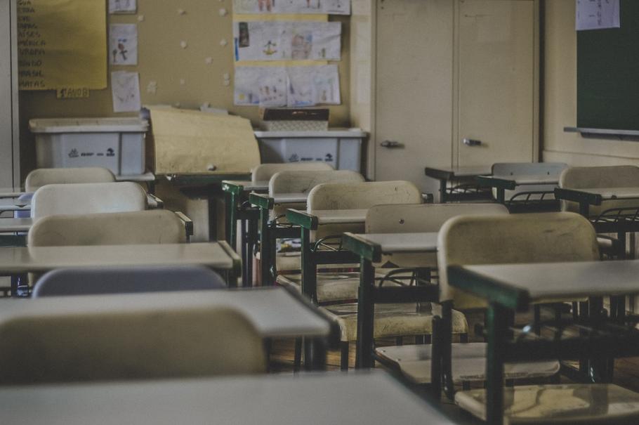 This is a photo of an empty classroom. There are rows of desks and in the back there is a bulletin board. The photo is dark and gives off a lonely, empty feeling.